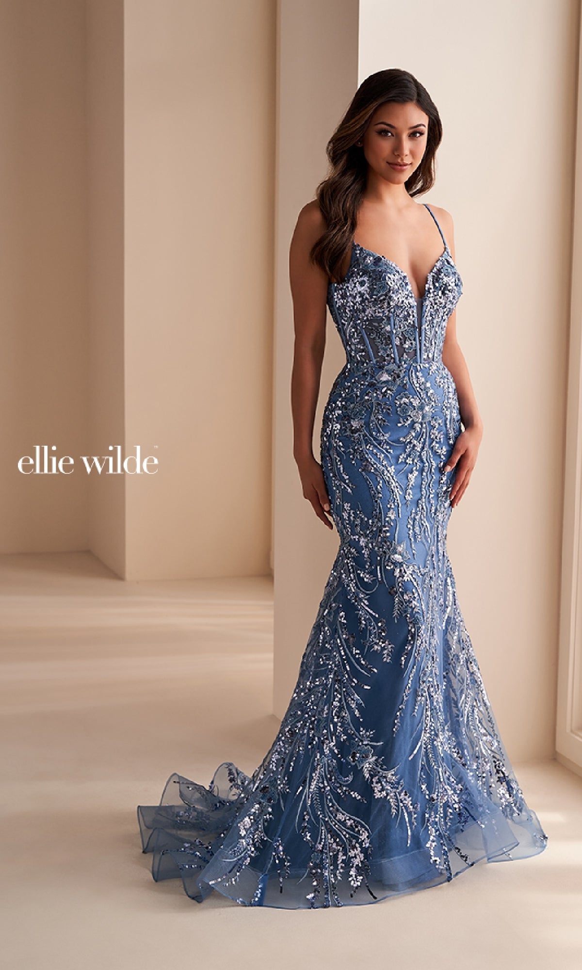 A woman stands indoors wearing the Ellie Wilde Long Black Sequin Prom Dress EW35039, which features a fitted silhouette, shimmering sequins, and elegant detailing for a striking prom look.